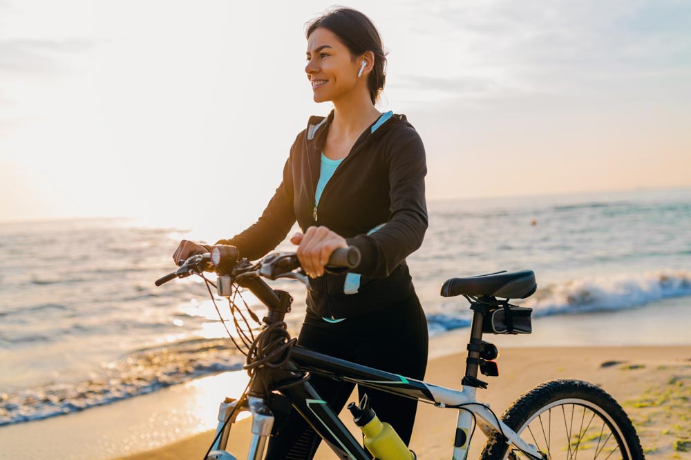young attractive slim woman riding bicycle, sports on morning sunrise beach in sports fitness sport clothes, active healthy lifestyle, smiling happy having fun